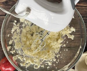 butter and cream cheese being beaten in a bowl with an electric hand mixer.