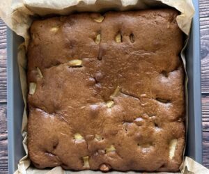 freshly baked apple spice cake with a golden top in a parchment lined square baking dish.