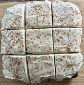cinnamon-dusted cream cheese frosted apple spice cake cut into 9 squares.