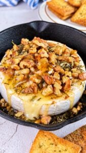 Honey baked Camembert topped with walnuts and herbs, with gooey melted cheese spilling over the rind.