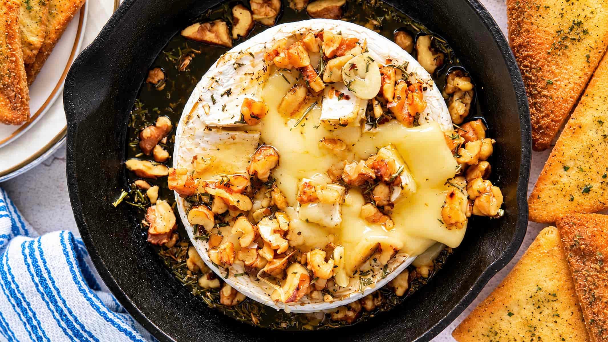 Gooey honey baked Camembert topped with walnuts, garlic, and herbs, served warm with golden toasted bread.