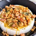 Honey baked Camembert topped with toasted walnuts, rosemary, and herbs in a cast-iron skillet.