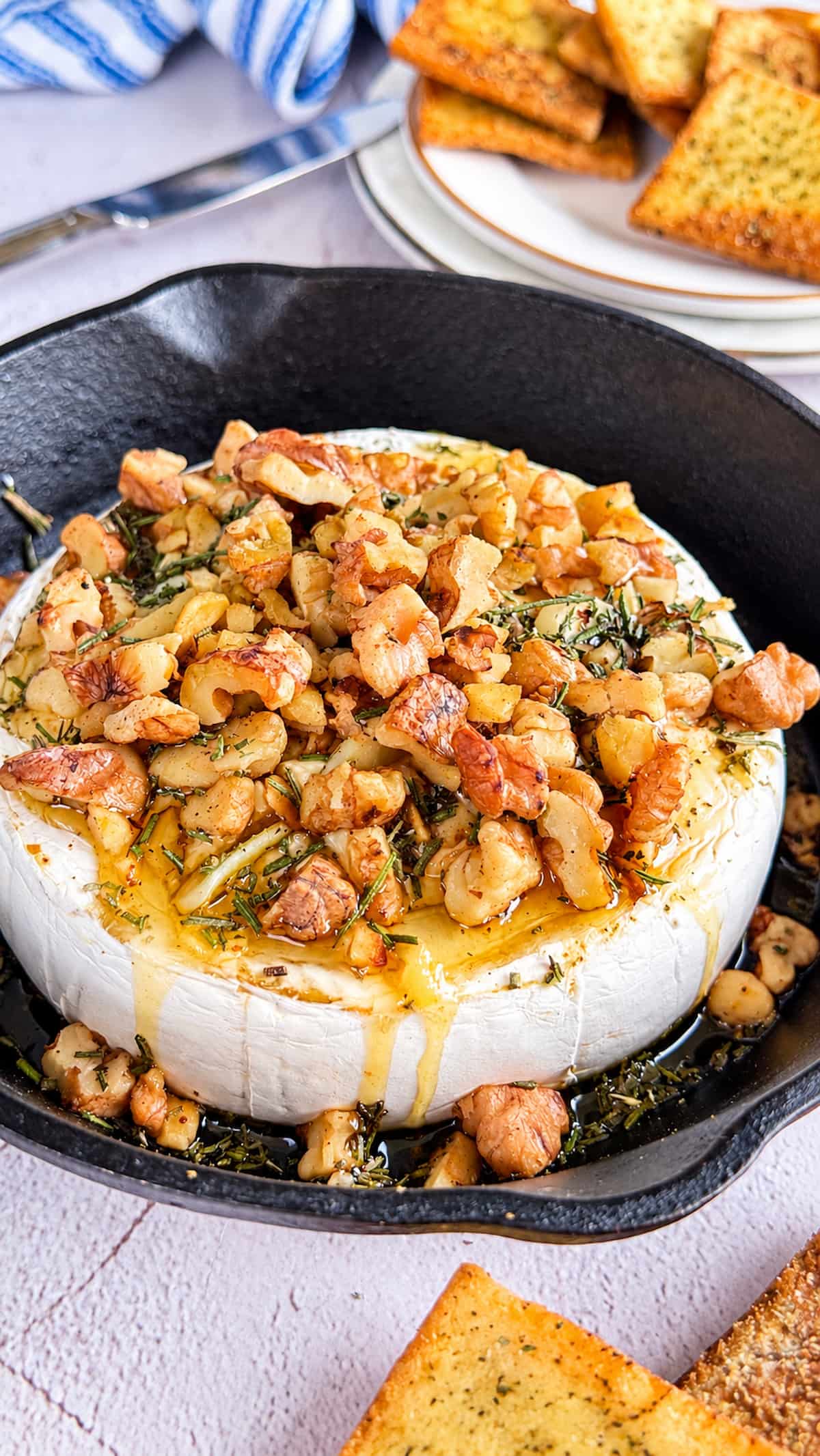 Honey baked Camembert topped with toasted walnuts, rosemary, and herbs in a cast-iron skillet.
