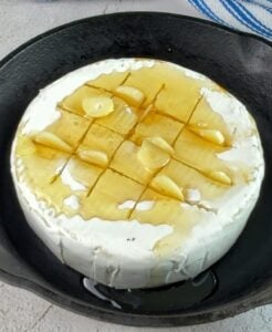 scored wheel of camembert cheese with sliced garlic in the scores and honey all over.