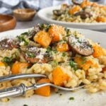 Side view of butternut squash and mushroom risotto on a plate with Parmesan, fresh herbs, and parsley.