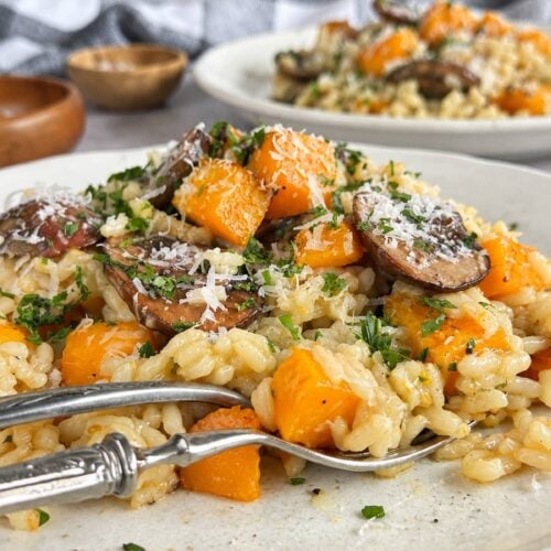 Side view of butternut squash and mushroom risotto on a plate with Parmesan, fresh herbs, and parsley.