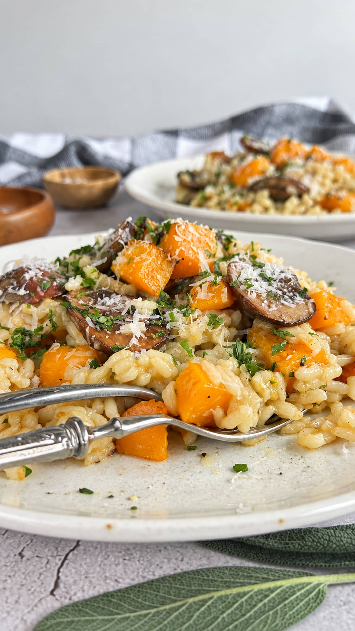 Side view of butternut squash and mushroom risotto on a plate with Parmesan, fresh herbs, and parsley.