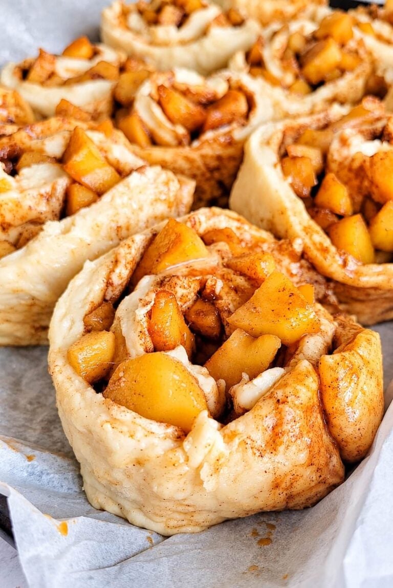 unbaked cinnamon and apple rolls on a parchment lined tray.