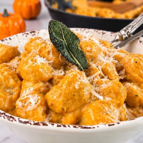 Creamy pumpkin gnocchi in a rich pumpkin sauce, topped with freshly grated Parmesan and crispy sage, served in a rustic bowl.