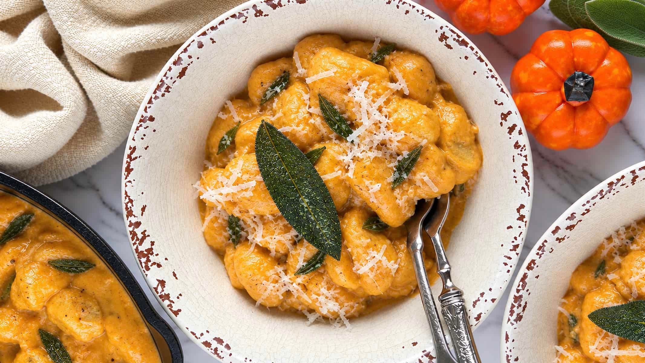 Creamy pumpkin gnocchi coated in a rich pumpkin sauce, topped with freshly grated Parmesan and crispy sage in a rustic bowl.