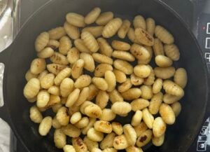 gnocchi toasting in a cast iron skillet on a burner.