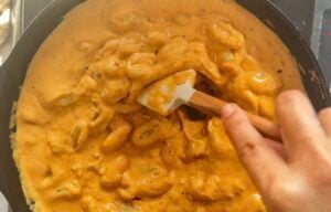 hand with a rubber spatula stirring gnocchi in pumpkin sauce in a skillet.