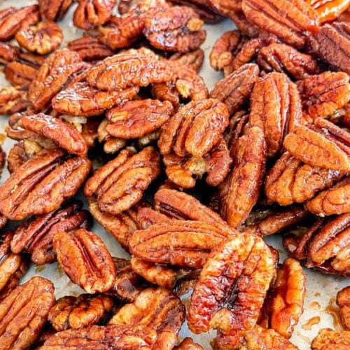 Homemade maple glazed pecans coated in a glossy maple syrup glaze, spread out on a baking sheet.