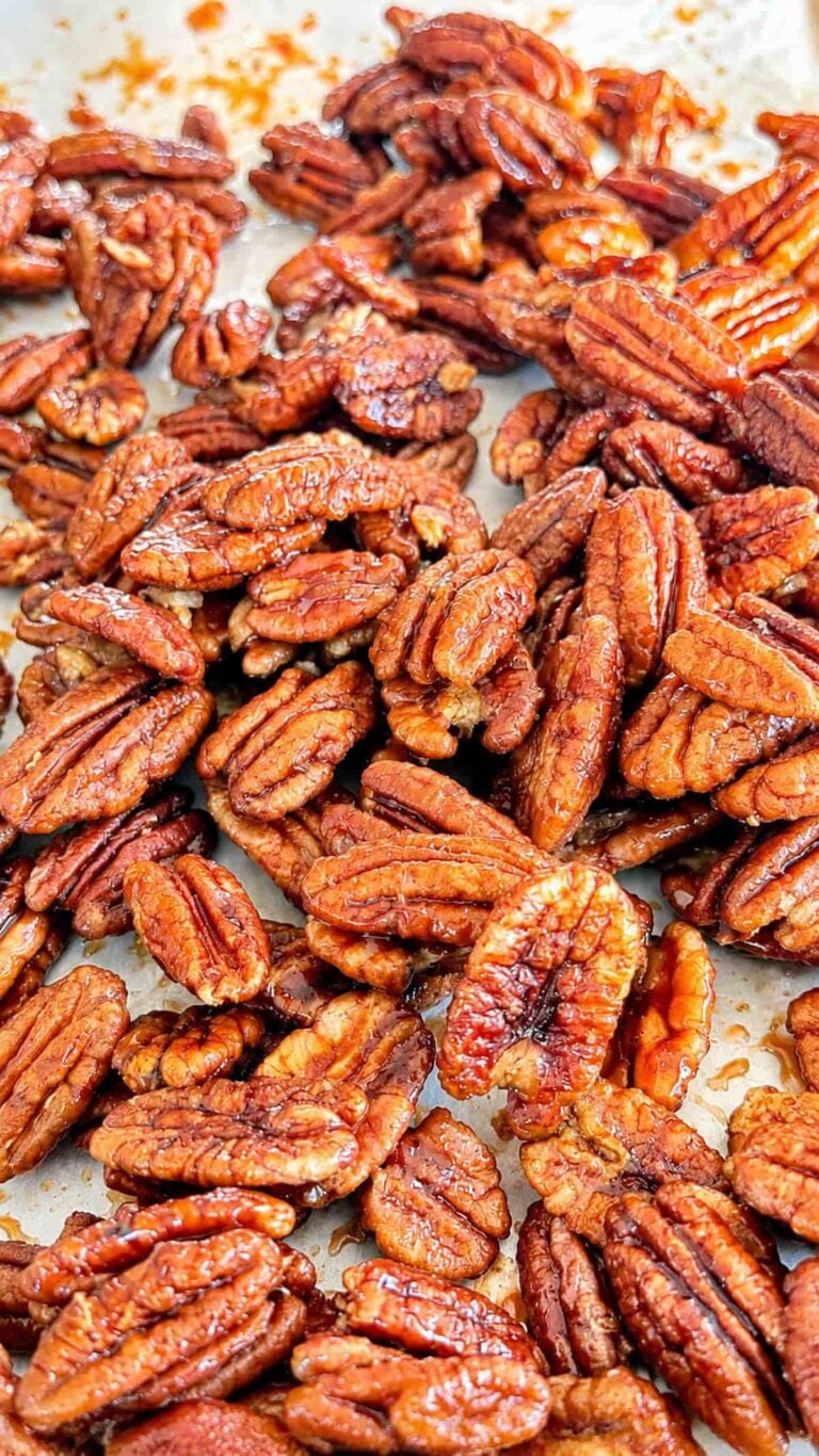 Homemade maple glazed pecans coated in a glossy maple syrup glaze, spread out on a baking sheet.