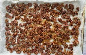 pecans in maple syrup spread out on a parchment lined baking sheet.