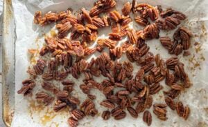 maple pecans spread out on a parchment lined baking sheet.