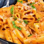 Creamy nduja rigatoni pasta with Parmesan, fresh basil, and red pepper flakes in a cast iron skillet.