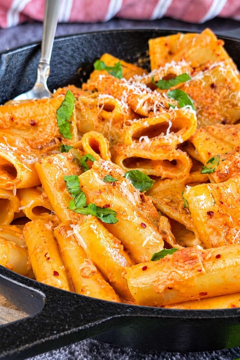 Creamy nduja rigatoni pasta with Parmesan, fresh basil, and red pepper flakes in a cast iron skillet.