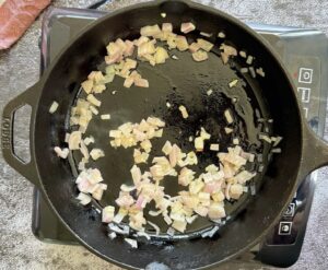 diced shallots cooking in oil in a cast iron skillet.