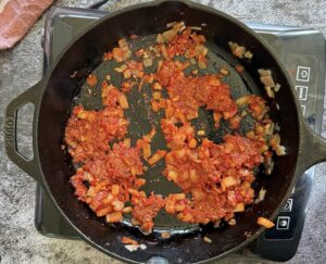 ndjua, tomato paste, and diced shallots cooking in a cast iron skillet.