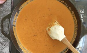 creamy orange sauce with a rubber spatula in a cast iron skillet.