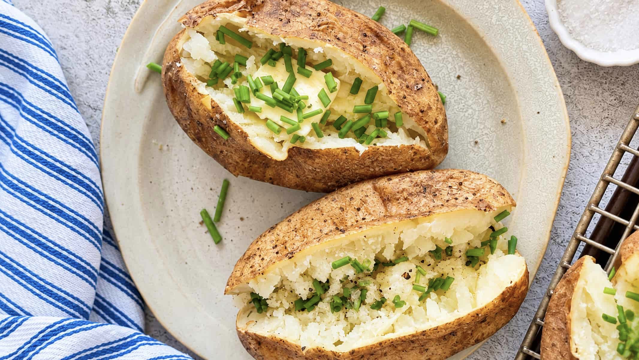 No foil baked potatoes with butter, fresh chives, salt, and black pepper on a ceramic plate.