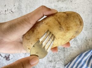 hand with a fork piercing a russet potato.