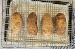4 salt and pepper seasoned baked potatoes on a wire rack and foil lined baking sheet.