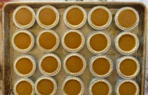 unbaked pumpkin pie tarts laid out in a single layer on a baking sheet.