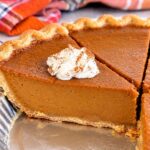 Homemade pumpkin pie slice with smooth, creamy pumpkin filling, flaky golden crust, and cinnamon-dusted whipped cream.