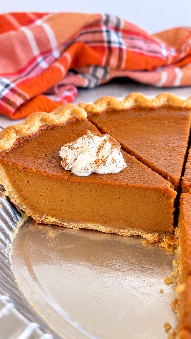 Homemade pumpkin pie slice with smooth, creamy pumpkin filling, flaky golden crust, and cinnamon-dusted whipped cream.