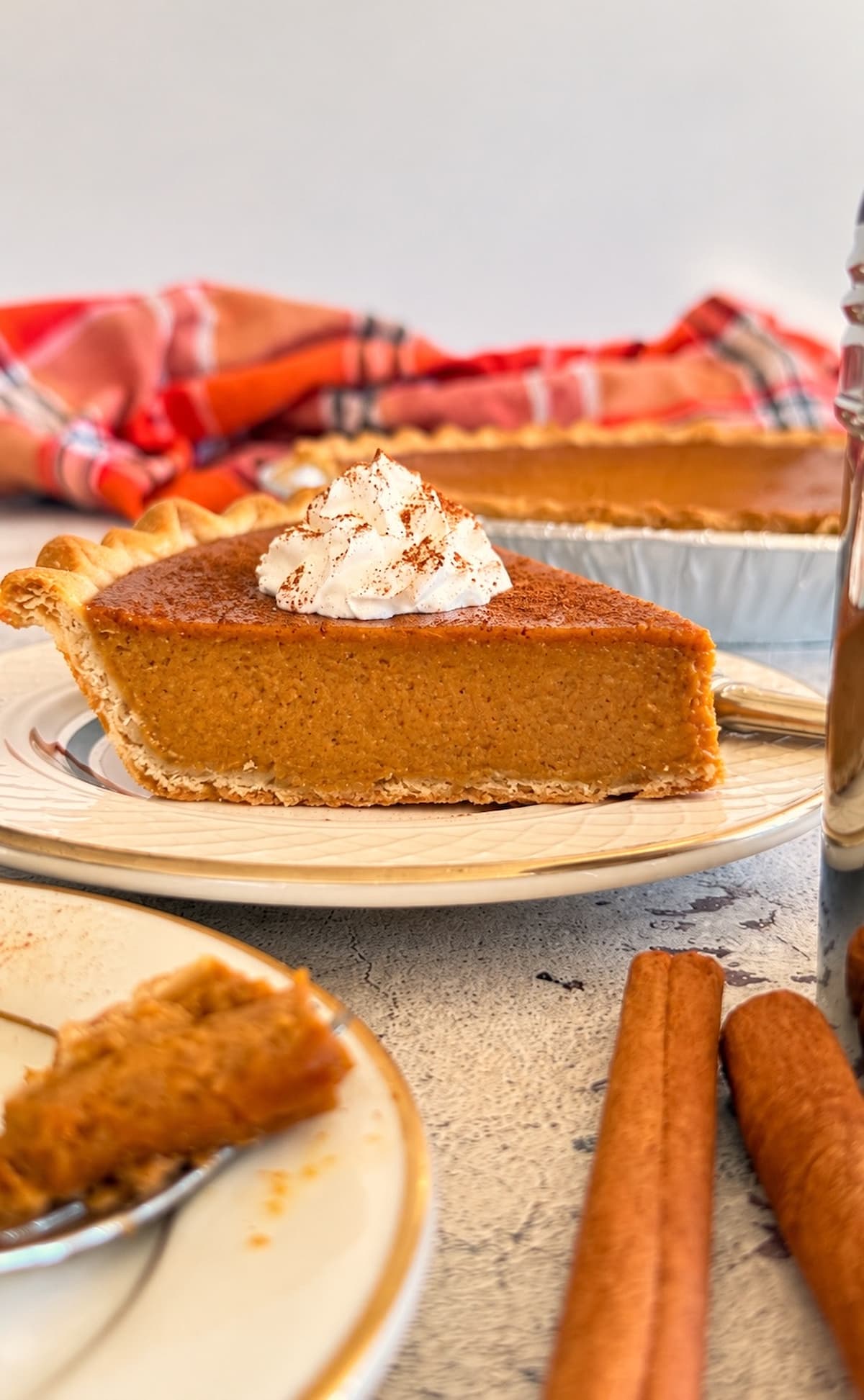 Homemade pumpkin pie slice with a flaky golden crust, topped with whipped cream and a sprinkle of cinnamon.