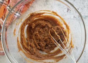 pumpkin pie filling being mixed in a large glass bowl with a whisk.