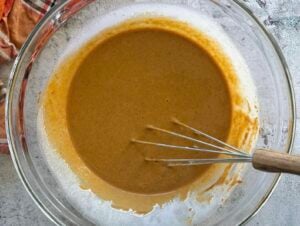creamy orange pumpkin pie filling in a large glass bowl with a whisk.